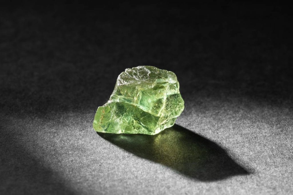 Translucent green Apatite crystal healing stone on dark background backlit from behind. Natural gemstone collection