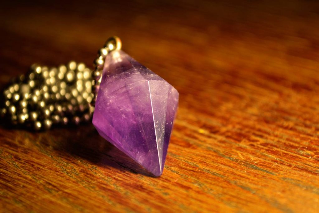 A closeup shot of a golden necklace with Amethyst stone on a wooden table