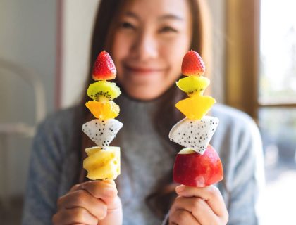 Closeup image of an asian woman holding and showing a fresh mixed fruits on skewers